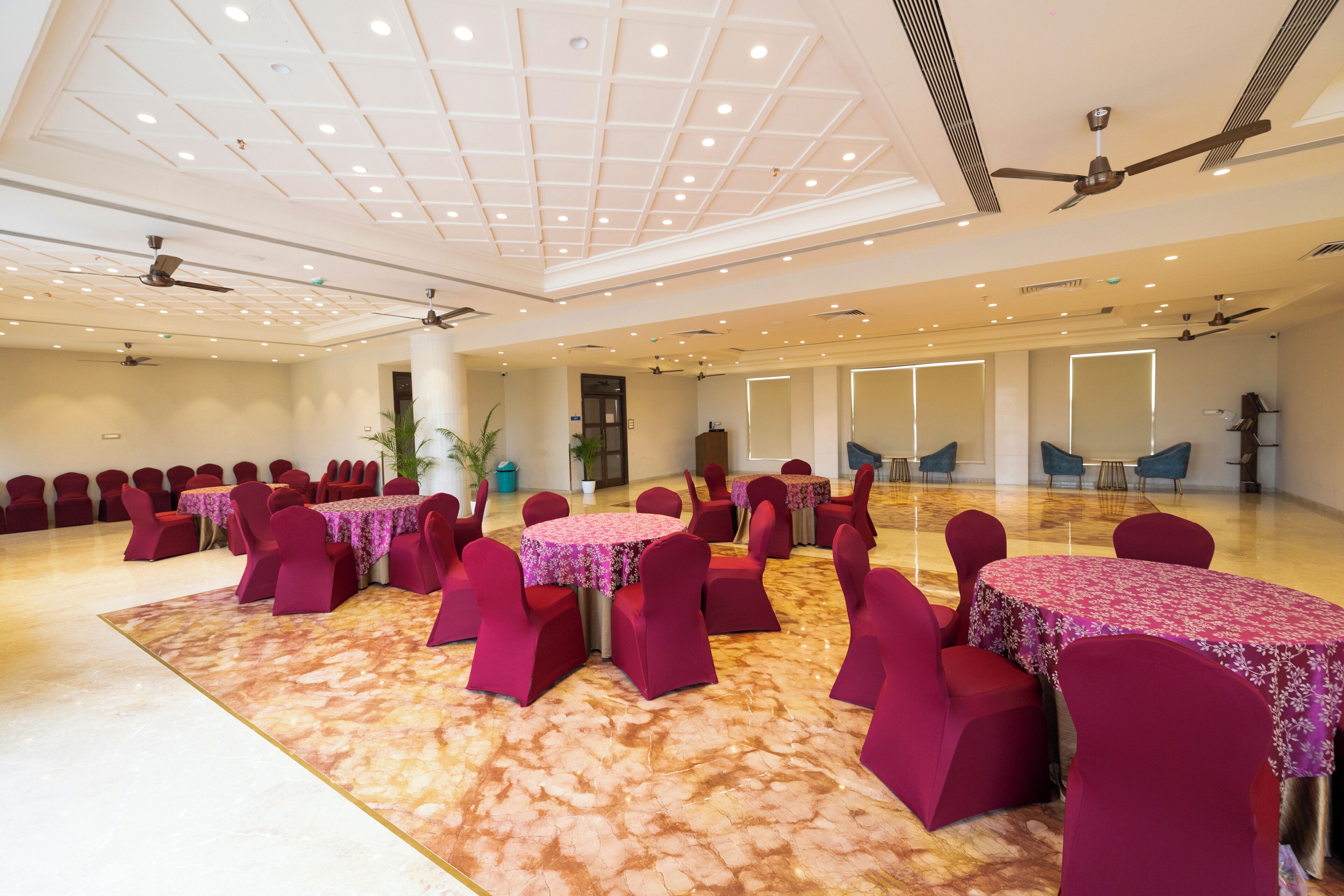 Un amplio salón de banquetes con varias mesas redondas cubiertas con manteles florales y rodeadas de sillas rojas.
