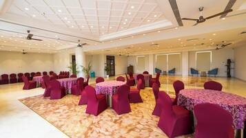 Un amplio salón de banquetes con varias mesas redondas cubiertas con manteles florales y rodeadas de sillas rojas.
