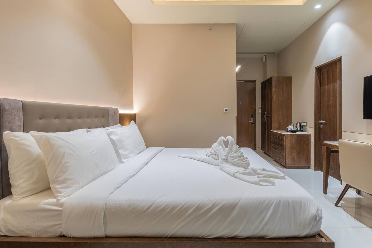 A neatly made bed with white linens, a headboard, and a set of towels on the bed.