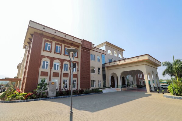 A multi-story building with a central entrance, a covered walkway, and a landscaped area with plants. - MAHARAJA AGRASEN PALACE - PURE VEGETARIAN (Mawal)
