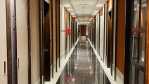A long, narrow hotel corridor with polished marble floors, wooden doors, and recessed lighting. - MAHARAJA AGRASEN PALACE - PURE VEGETARIAN (Mawal)