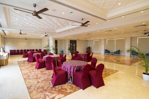 A spacious banquet hall with multiple round tables, red chairs, ceiling fans, and a polished marble floor. - MAHARAJA AGRASEN PALACE - PURE VEGETARIAN (Mawal)