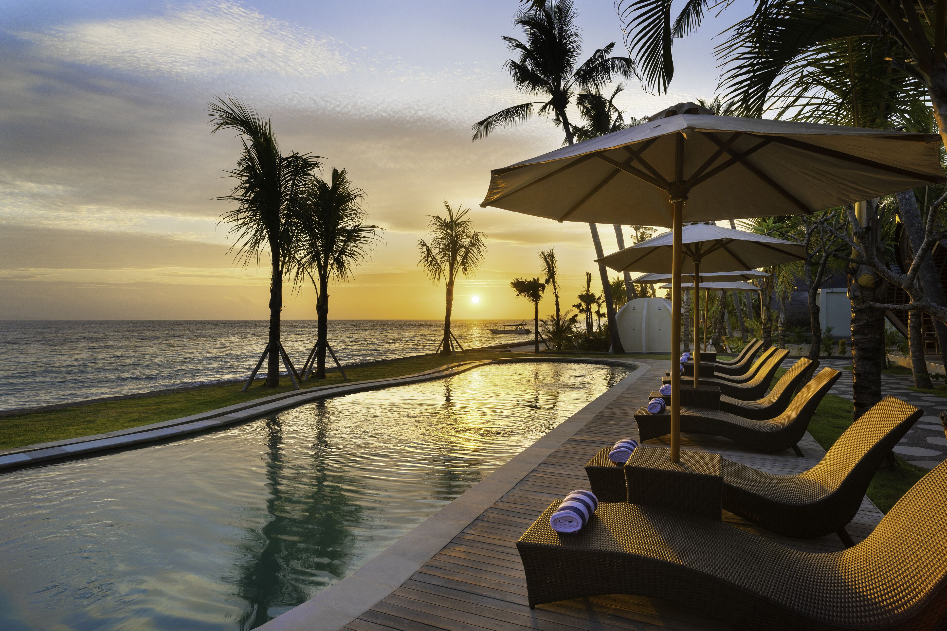 A poolside area with lounge chairs and umbrellas, overlooking a body of water with palm trees.