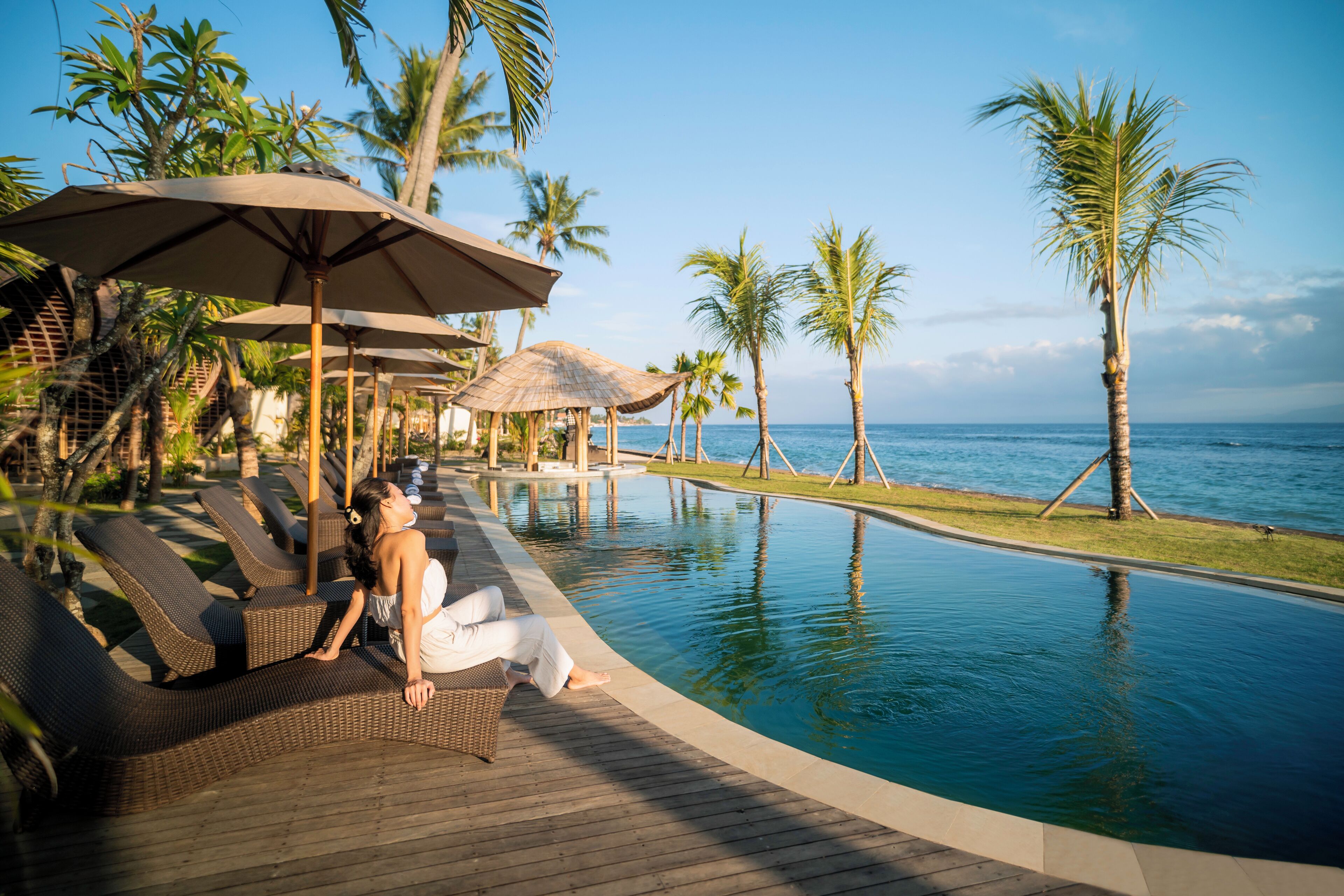 A poolside area with lounge chairs and umbrellas, overlooking a clear blue ocean.