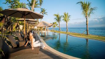 A poolside area with lounge chairs and umbrellas, overlooking a clear blue ocean.