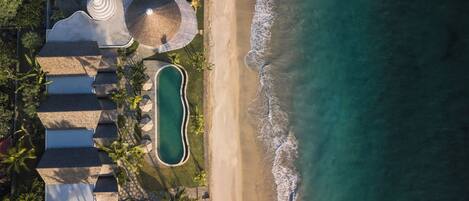 An aerial view of a resort with a swimming pool, beach, and multiple buildings with a circular structure.