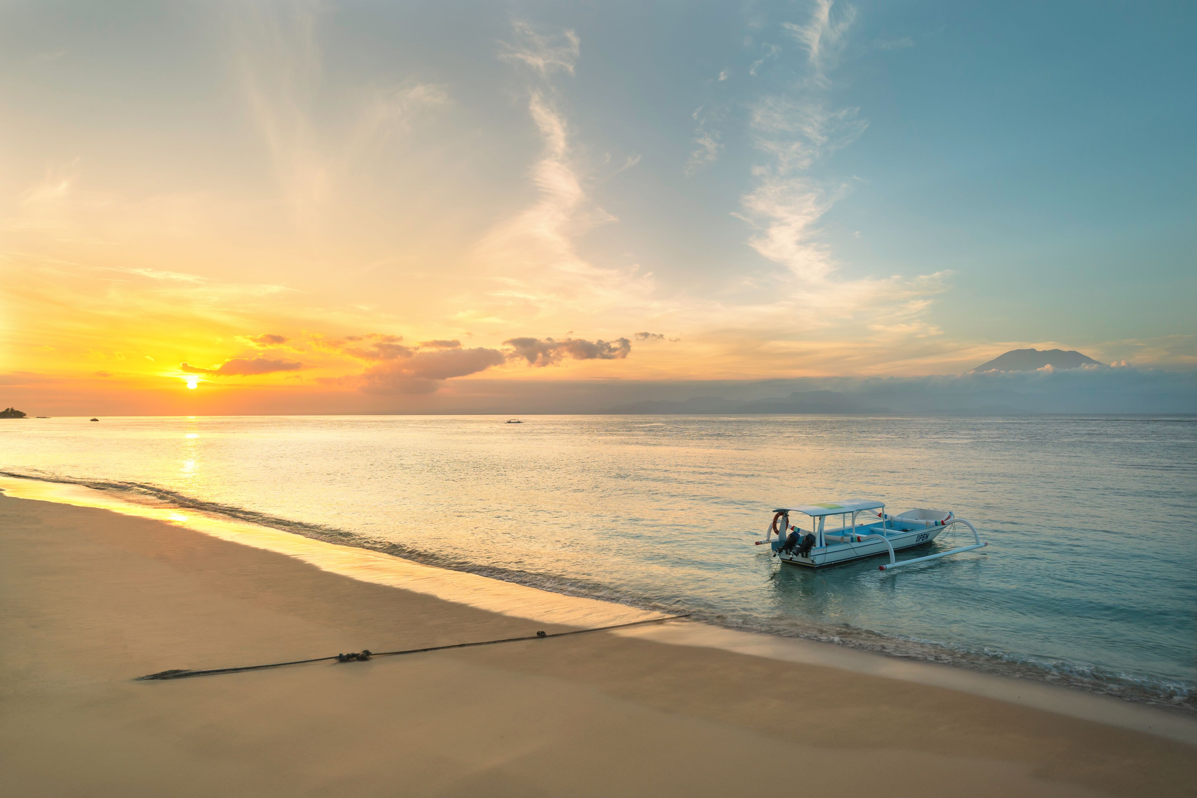 Un barco sobre un mar tranquilo al atardecer, con una montaña de fondo.
