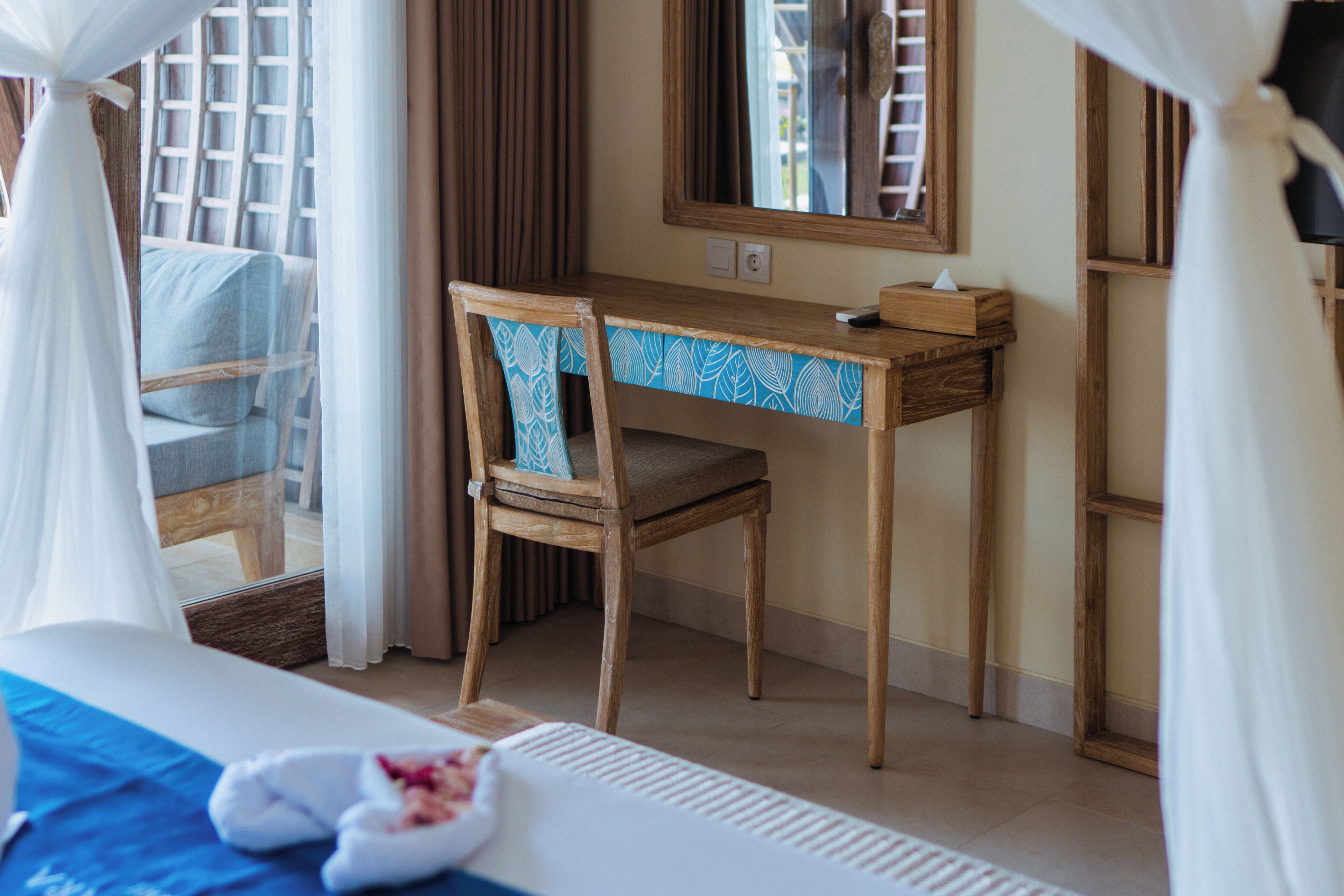 A bedroom with a bed, a wooden desk, a chair, and a window with curtains.