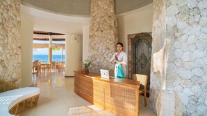 A reception area with a stone wall, a receptionist, and a view of the ocean. - The Sankara Beach Penida (Penida Island)