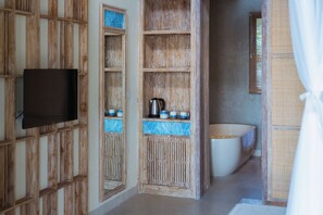 A room with a television mounted on a wooden wall, a shelf with kitchen items, and a large white bowl.
