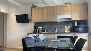 A modern kitchen with wooden cabinets, a black countertop, a built-in microwave, and a dining area with a table and chairs. - La vie est belle - Arromanches center, terrace (Arromanches-les-Bains)