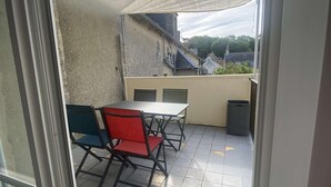 A patio area with a table and chairs, a trash bin, and a view of buildings in the background. - La vie est belle - Arromanches center, terrace (Arromanches-les-Bains)