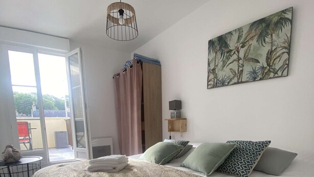 A hotel room with a large bed, a ceiling fan, a painting of tropical foliage, and a view through a glass door. - La vie est belle - Arromanches center, terrace (Arromanches-les-Bains)