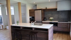 A modern kitchen with a central island, wooden stools, a microwave, and a coffee machine. - AKATSUKI (Furano)