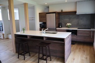 Uma cozinha moderna com uma ilha central, banquetas de madeira, micro-ondas e máquina de café.
