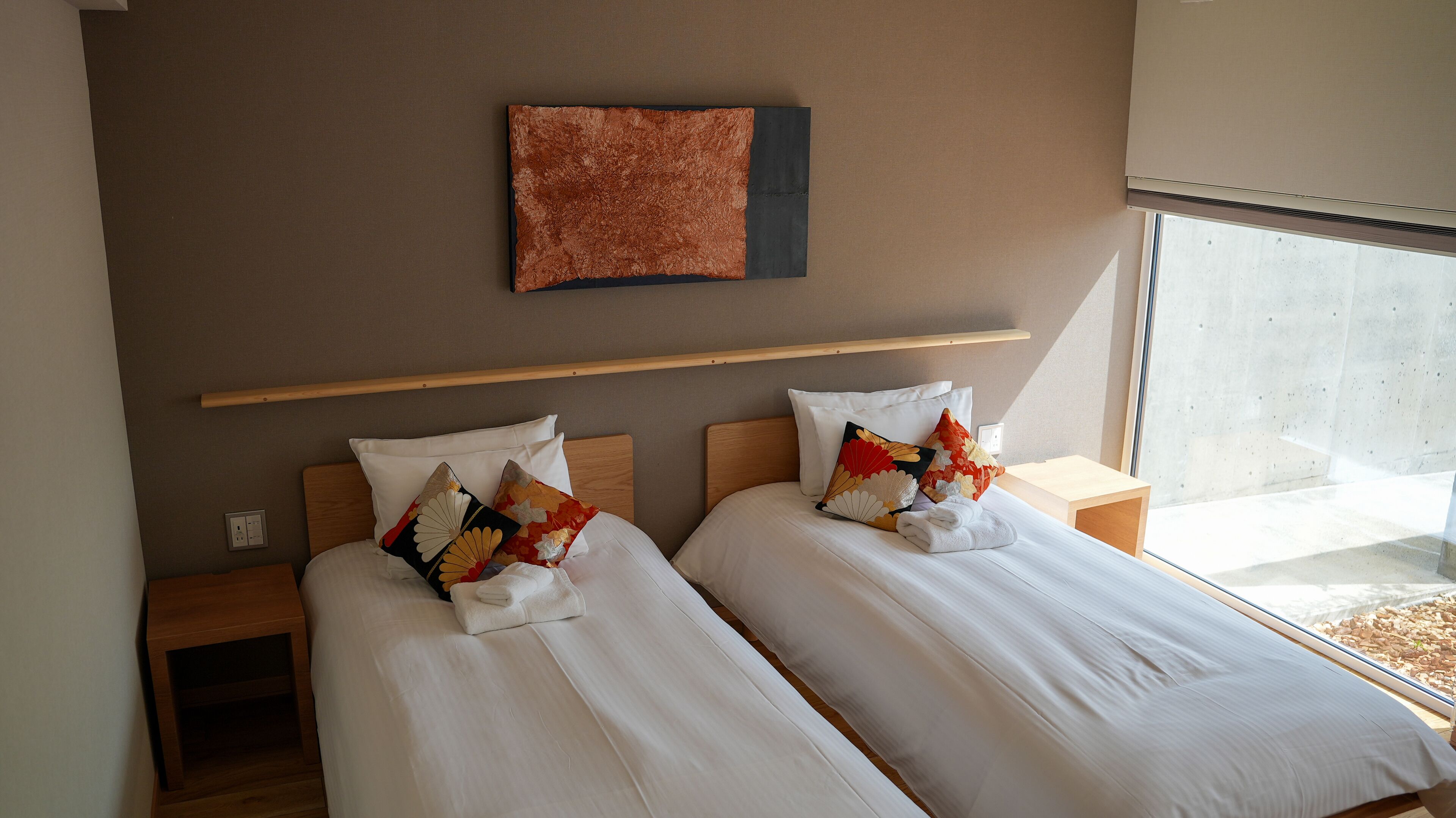 A hotel room with two beds, a wooden headboard, a wall-mounted artwork, and a window with a view.
