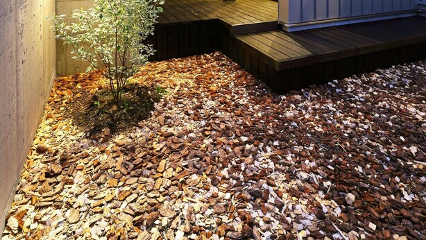 A modern house with a concrete exterior, a wooden deck, and a small garden area with mulch and a tree. - AKATSUKI (Furano)