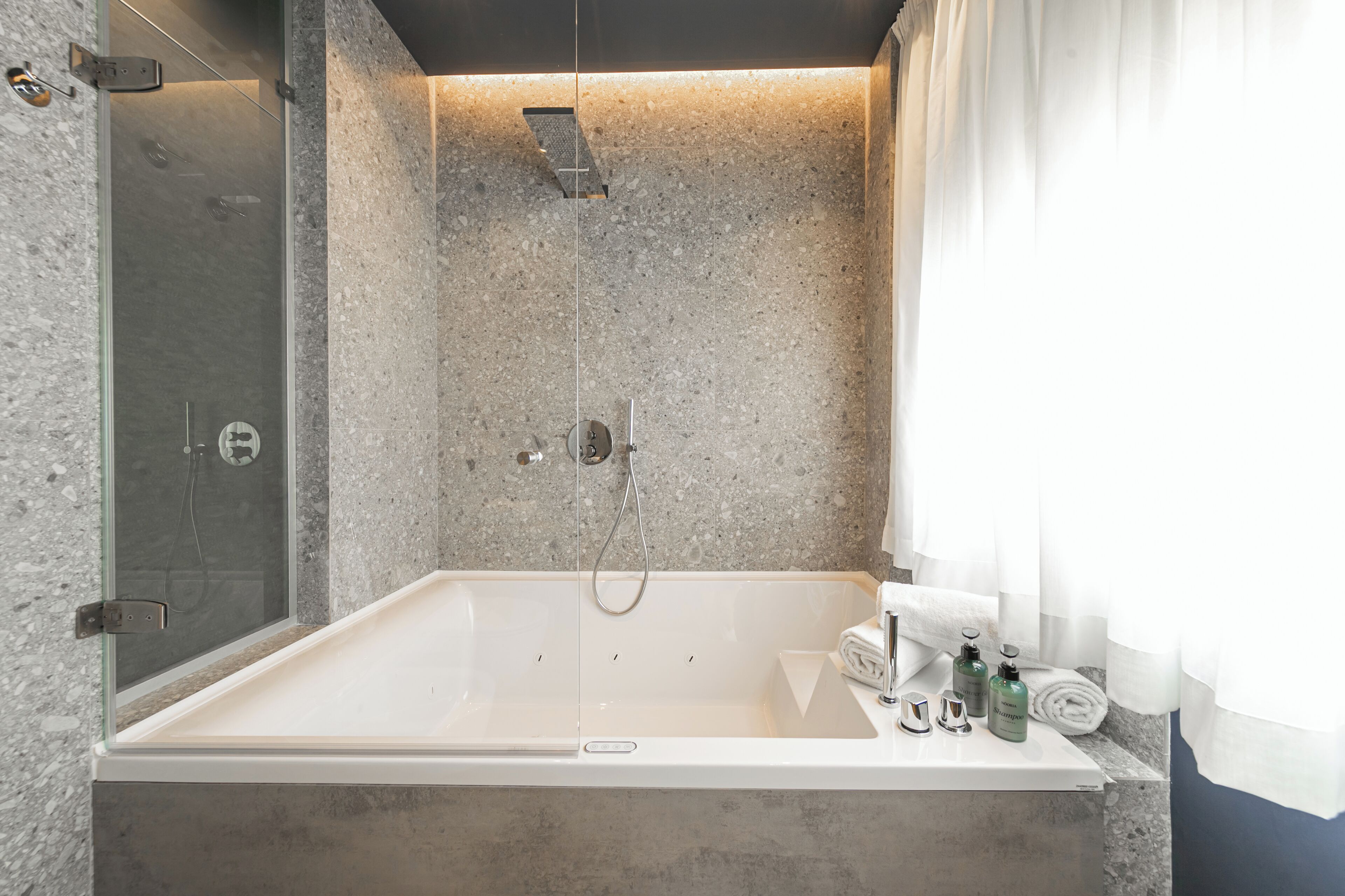 Un baño moderno con una bañera independiente, ducha envuelta en vidrio y pared con azulejos de mármol.