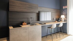 A modern kitchen with a built-in island, bar stools, a sink, and a flat-screen TV. - Nooria Sicilian Charme Rooms (Cefalù)