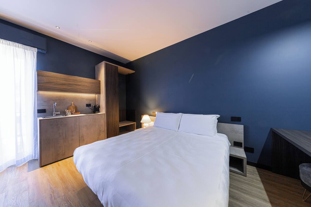 Ein modernes Hotelzimmer mit einem großen Bett, einem fest eingebauten Schreibtisch und einem Nachttisch mit Lampe.