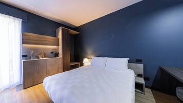 A modern hotel room with a large bed, a built-in desk, and a bedside table with a lamp.