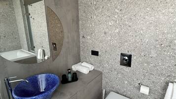 A modern bathroom with a blue vessel sink, a white toilet, and a grey vanity.