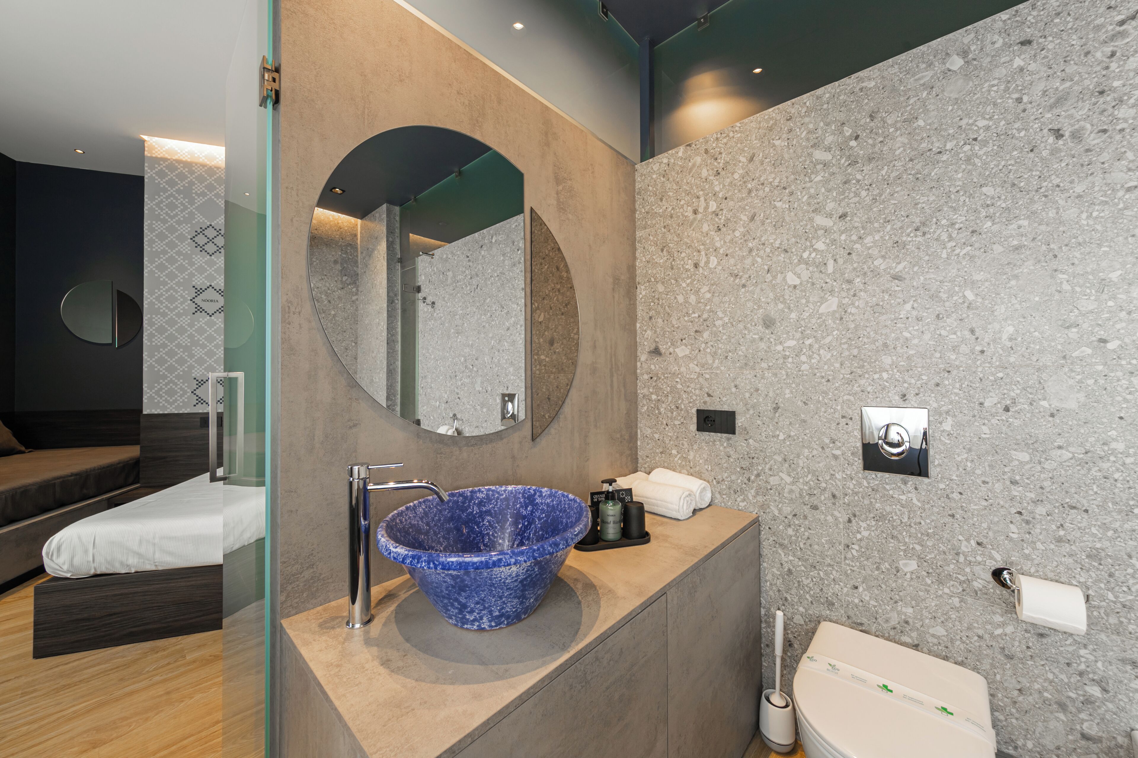 A modern bathroom with a large blue sink, a round mirror, and a toilet.