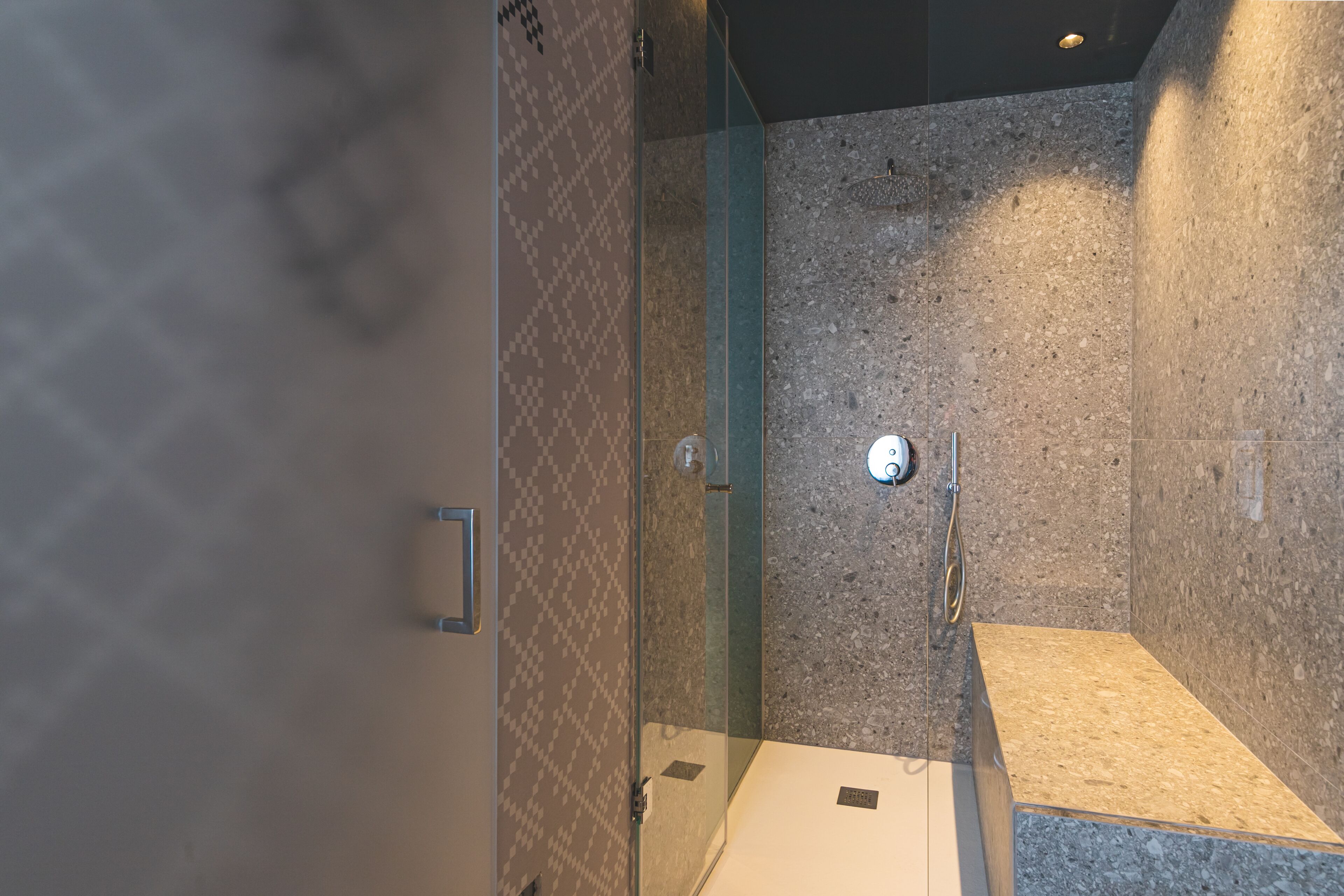 Eine gläserne Dusche mit Wand aus Granit, Bedienfeld und gefliestem Boden.