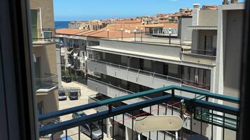 A balcony with a view of a residential area, including buildings and parked cars.
