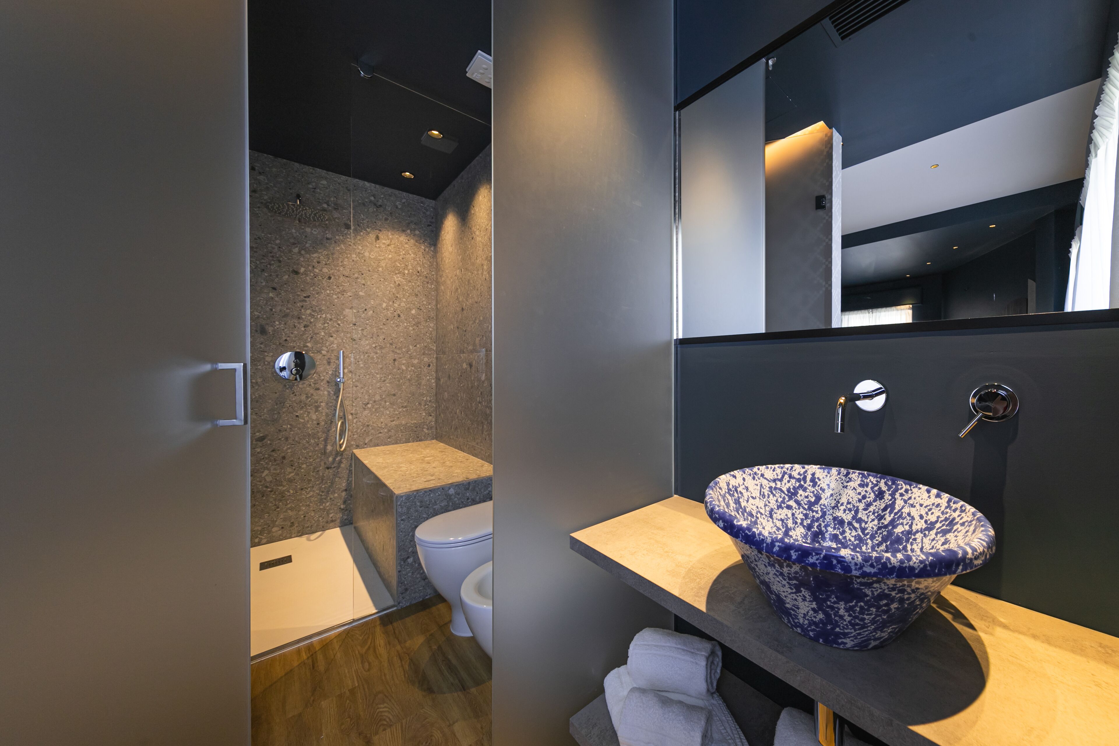 A modern bathroom with a glass-enclosed shower, a white toilet, and a blue and white patterned sink.