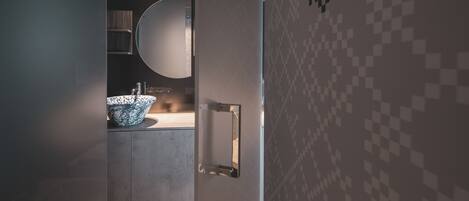 A modern bathroom with a large, round mirror, a white sink, and a tiled wall with a geometric pattern.