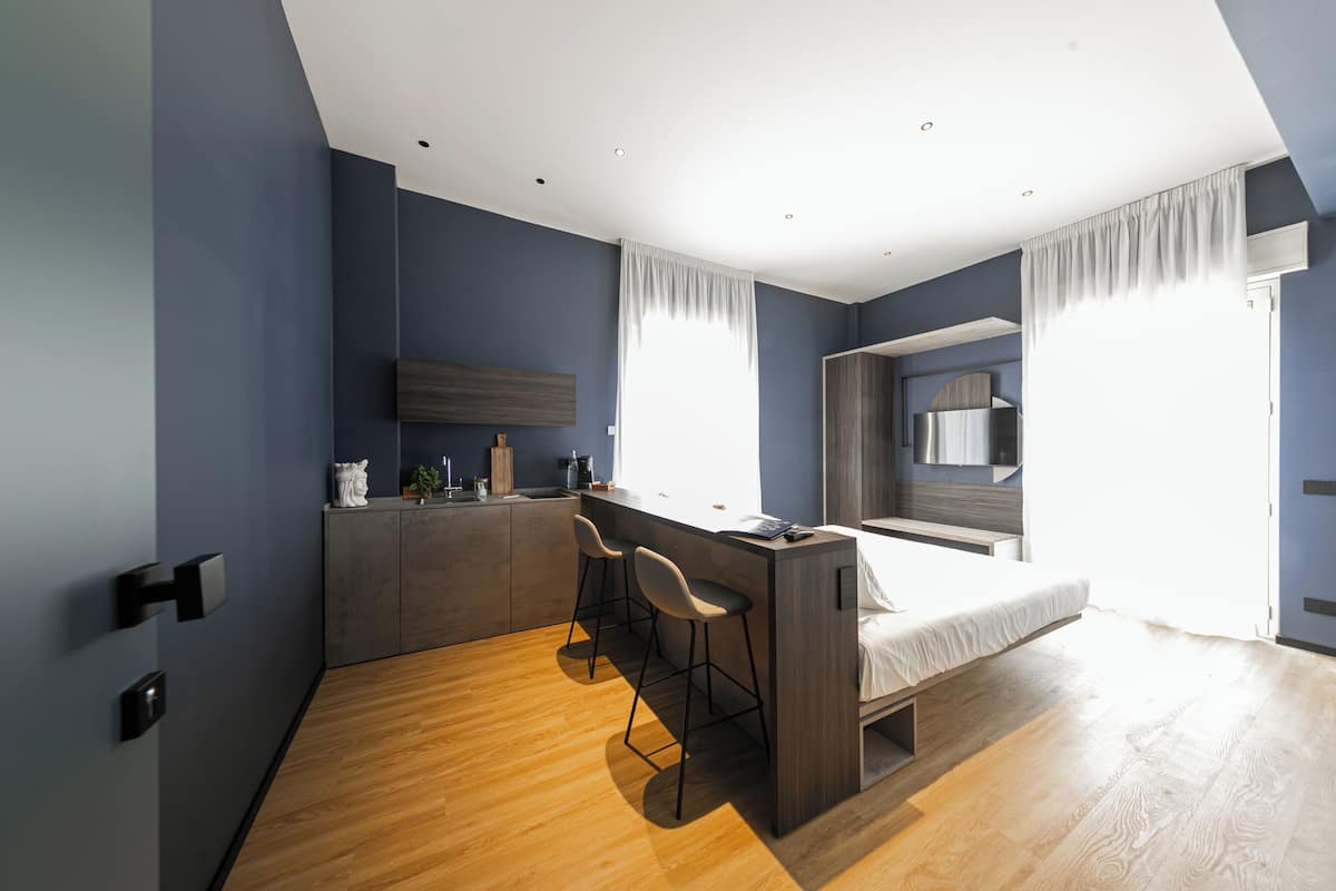 Ein modernes Schlafzimmer mit Bett, einer kleinen Küchenzeile und einem Fenster mit Vorhängen.