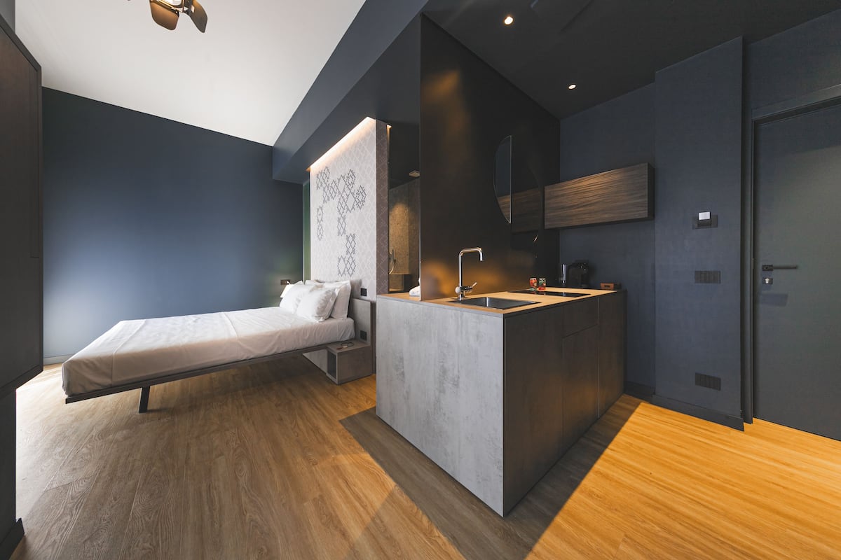 Ein modernes Schlafzimmer mit einem Bett, einem kleinen Schreibtisch und einer integrierten Küchenzeile mit Spüle und Arbeitsplatte.