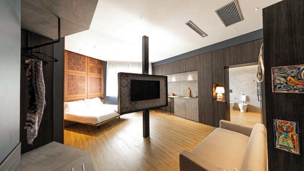 A modern hotel room with a large bed, a TV, a desk, and a bathroom. - Nooria Sicilian Charme Rooms (Cefalù)