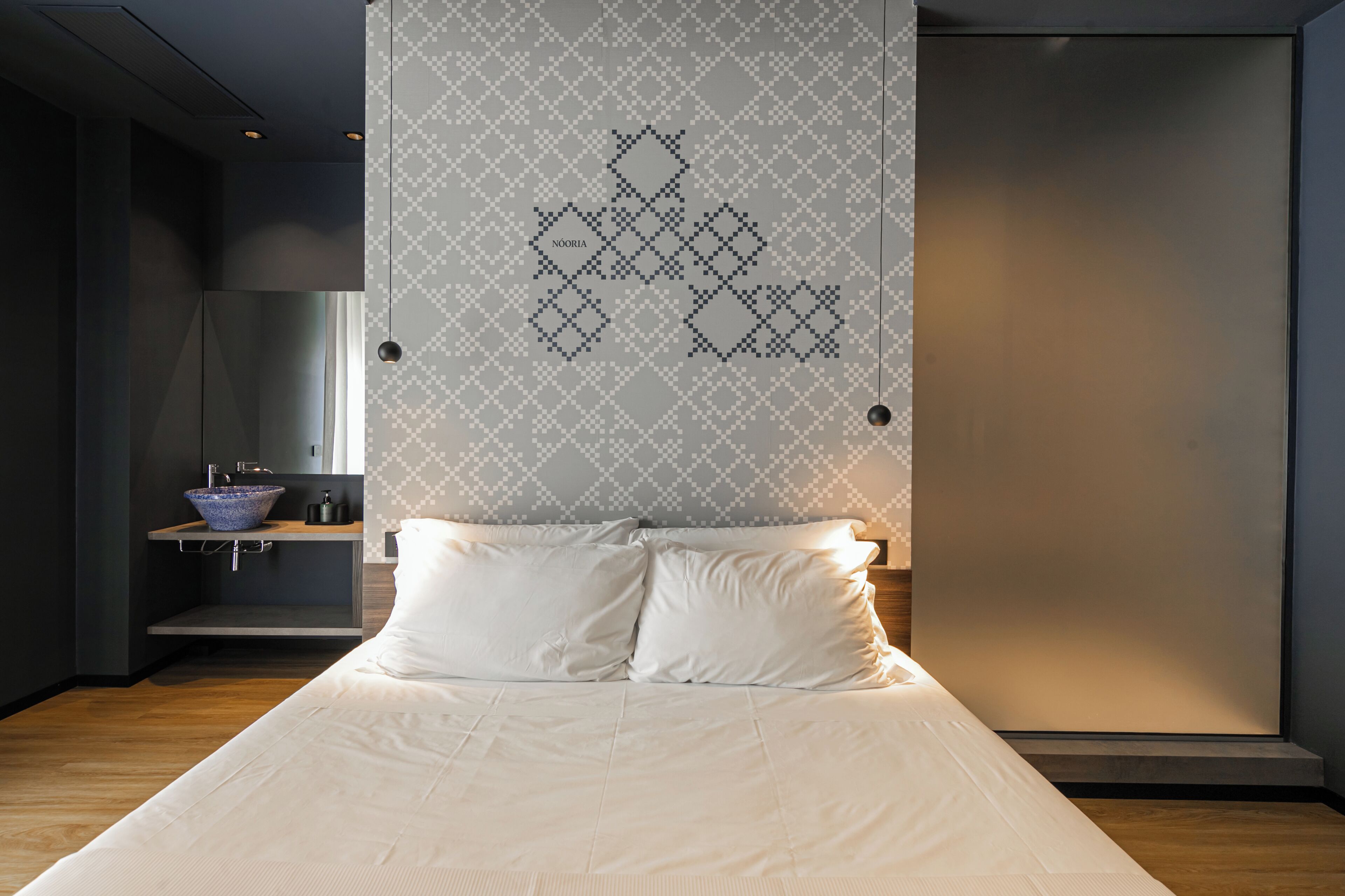 Un dormitorio moderno con una cama grande, una mesita de noche con un tazón azul y una pared con diseño geométrico.