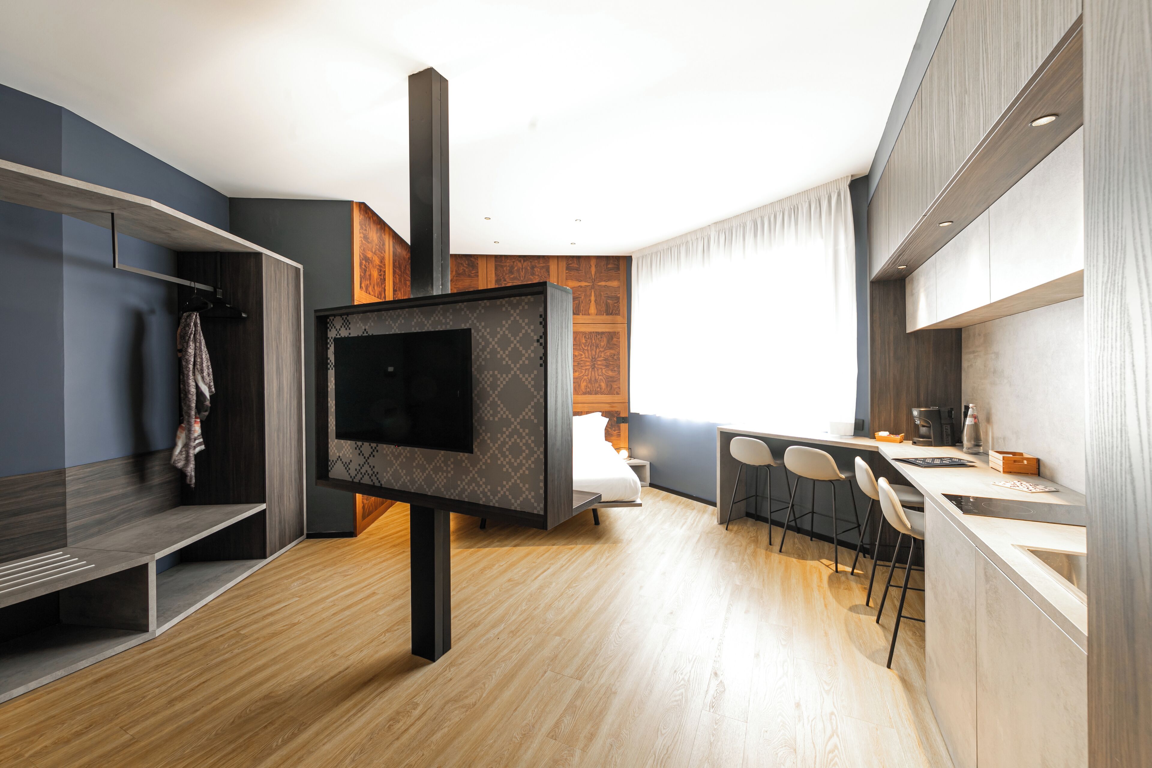 A modern kitchen with a built-in stove, a dining area with bar stools, and a large flat-screen TV mounted on a wooden wall.