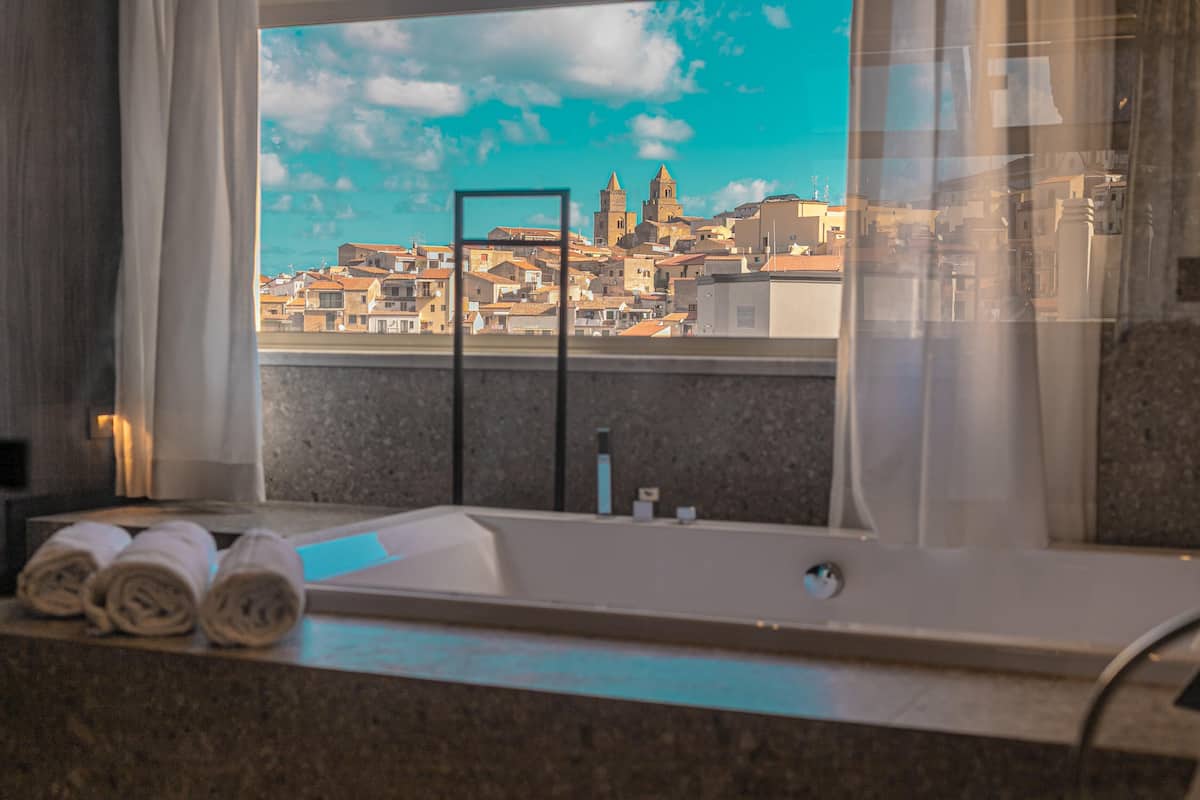 Ein Badezimmer mit Badewanne, Handtüchern und einem Fenster mit Blick auf die Stadt.