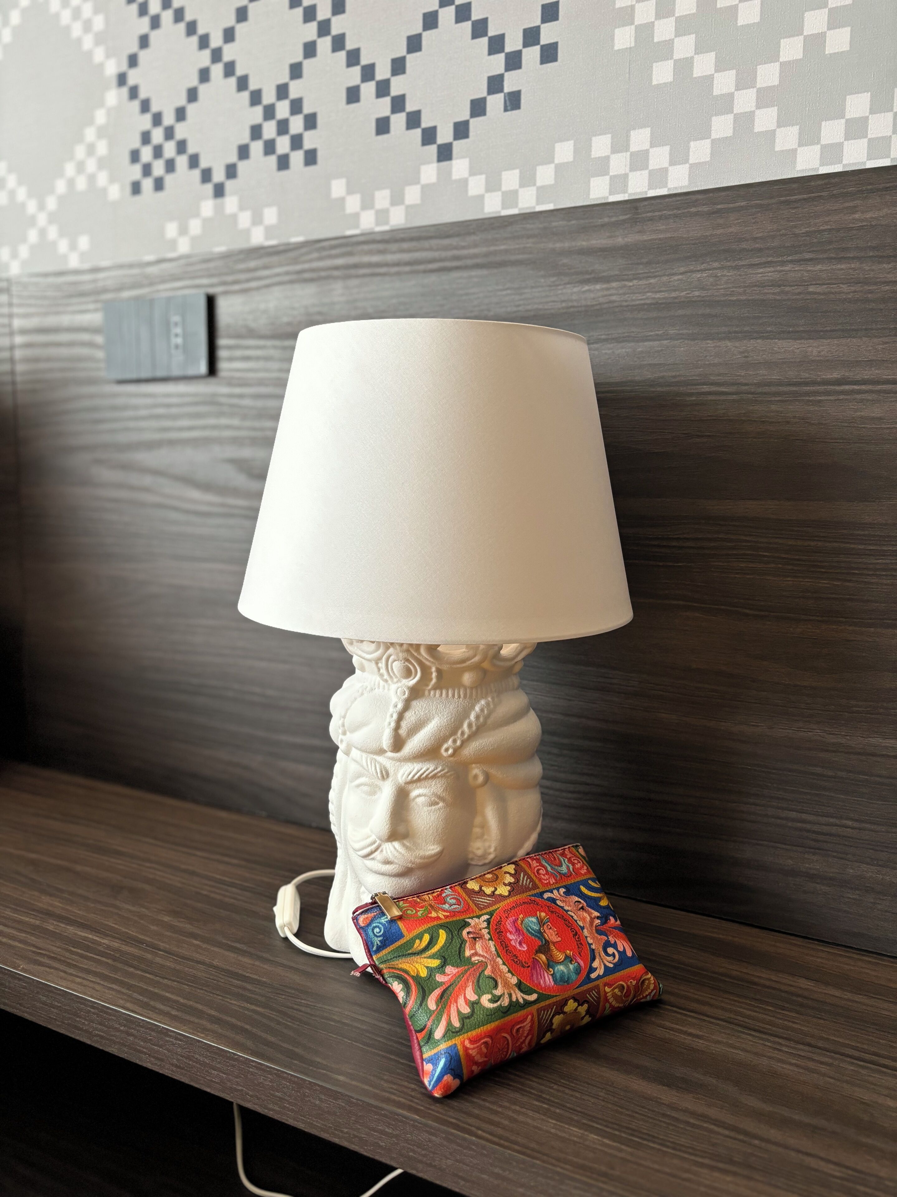 Een witte bureaulamp met decoratieve voet op een houten bank.