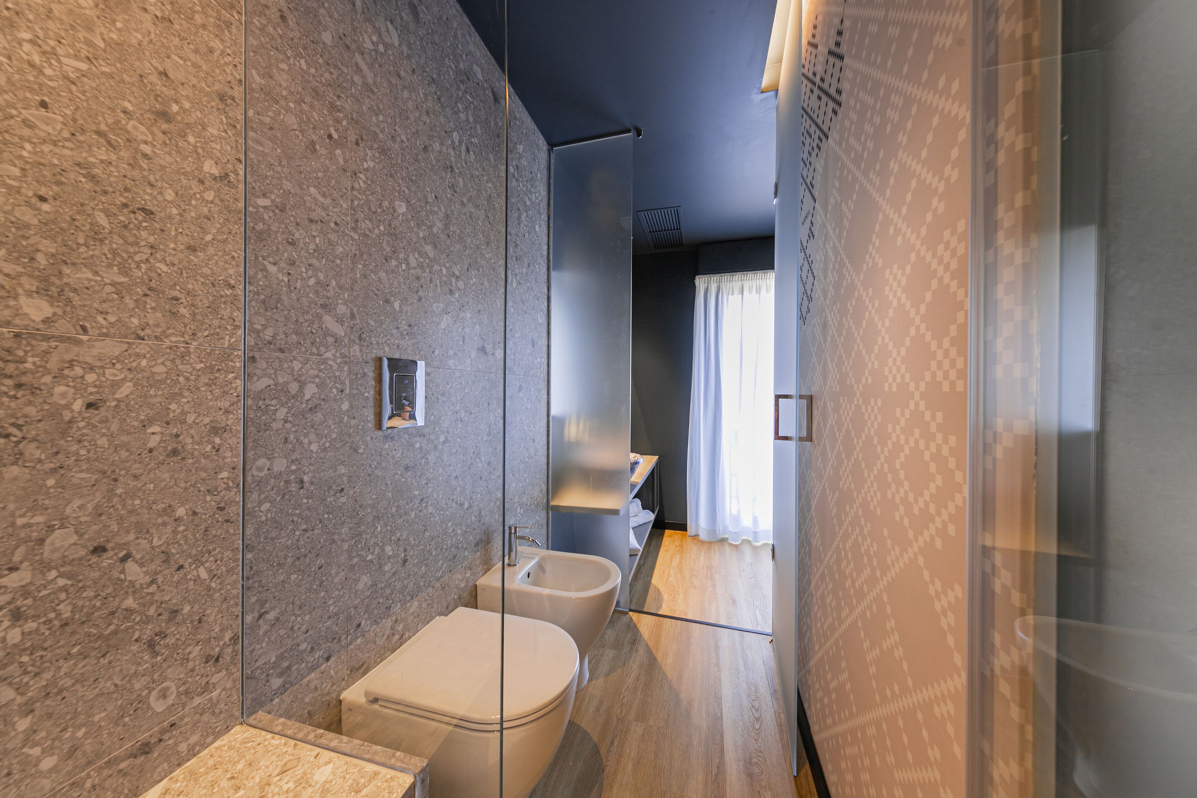 A modern bathroom with a marble wall, a glass shower enclosure, and a wooden floor.