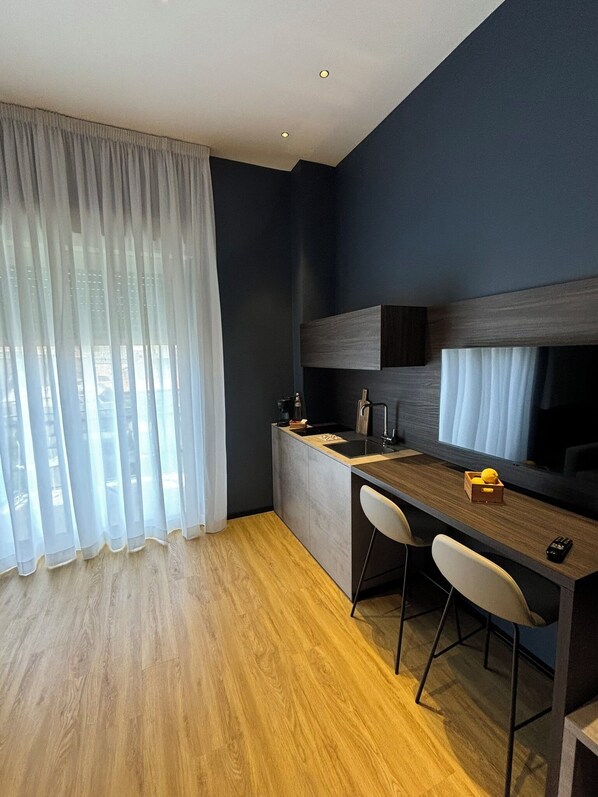 Una cocina moderna con encimera de madera, dos taburetes de bar, un fregadero y una ventana con cortinas translúcidas.