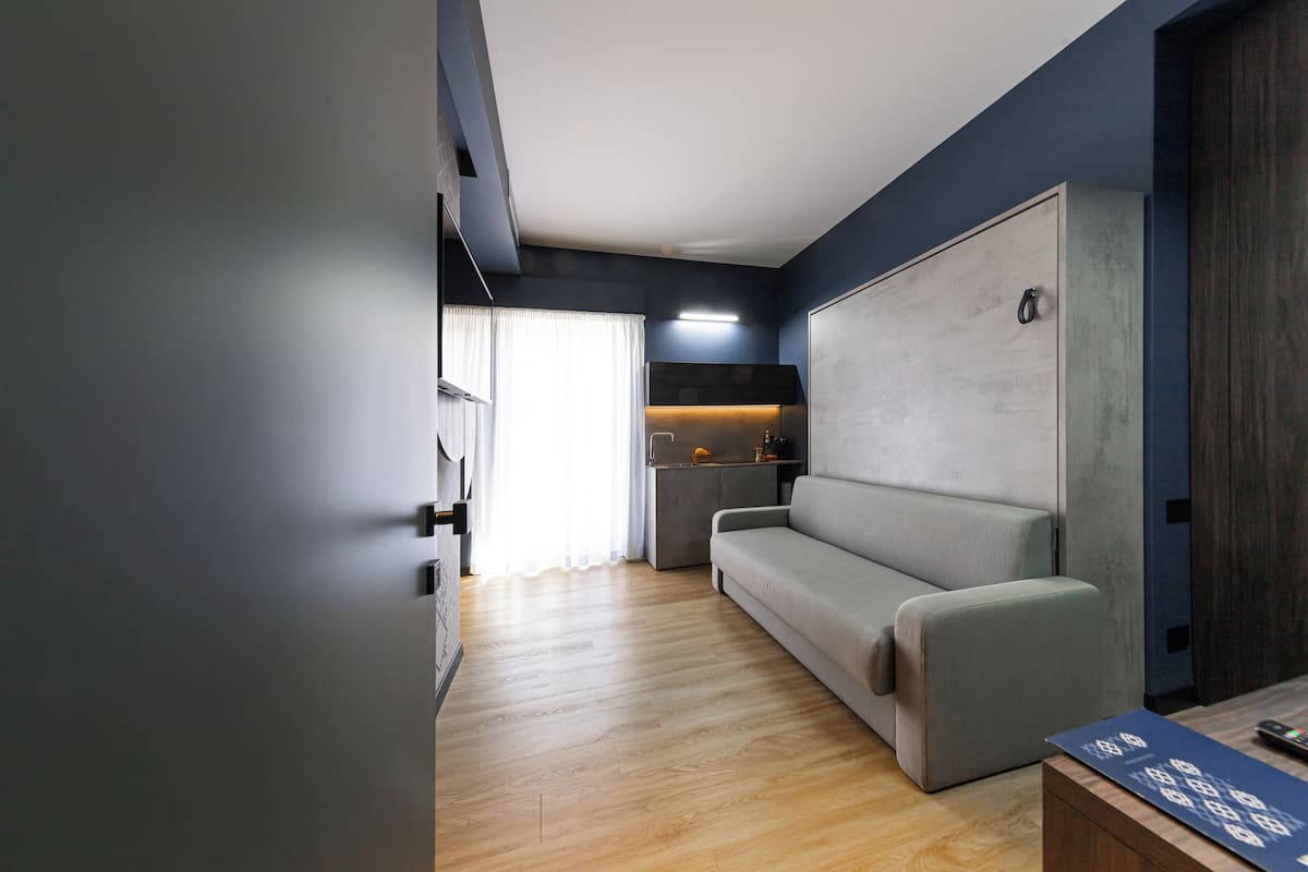 Ein modernes Wohnzimmer mit einem grauen Sofa, Holzboden und einer integrierten Küchenzeile mit Arbeitsplatte und Schränken.