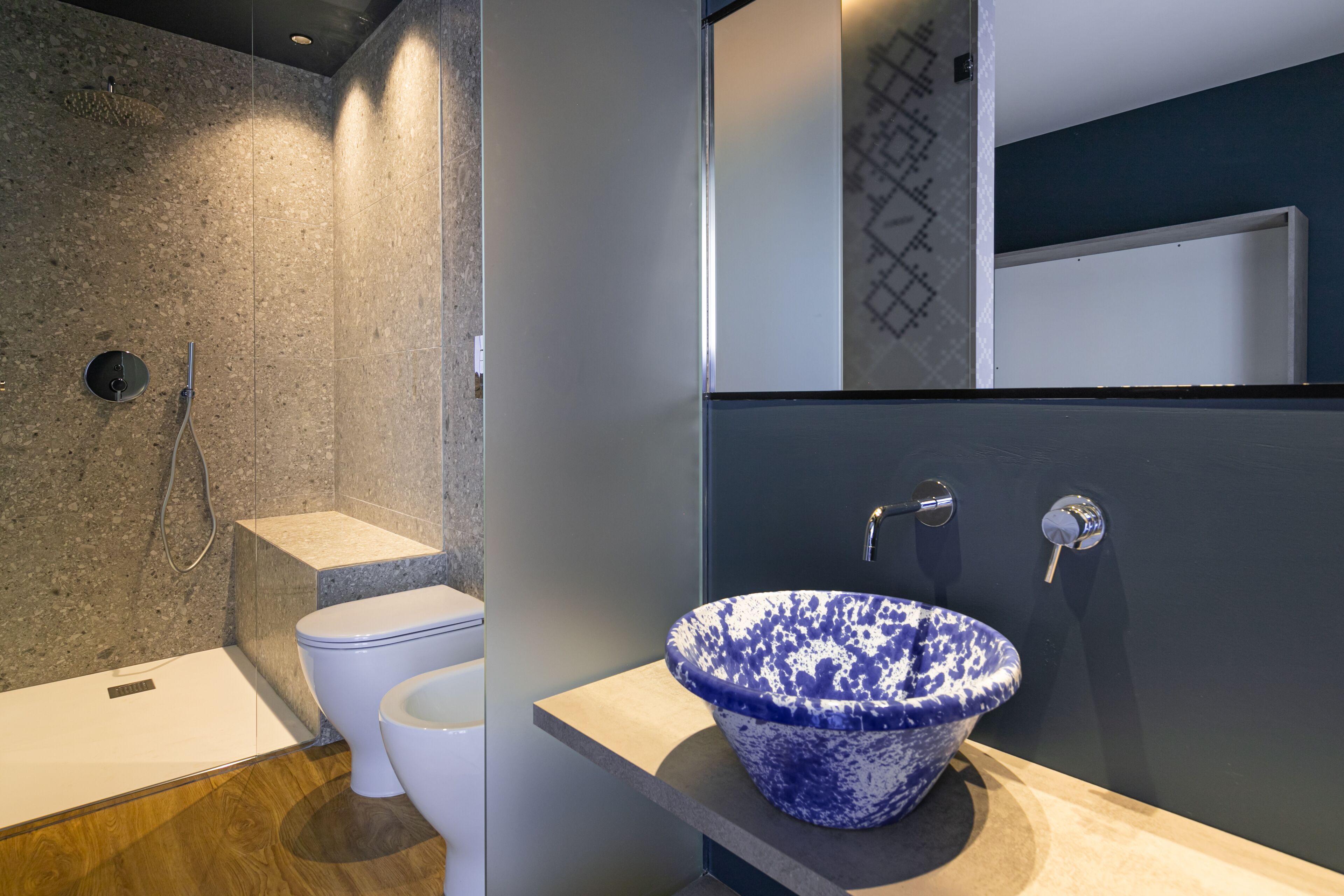 Un baño moderno con un inodoro independiente, ducha integrada y un lavamanos grande con estampado azul y blanco.
