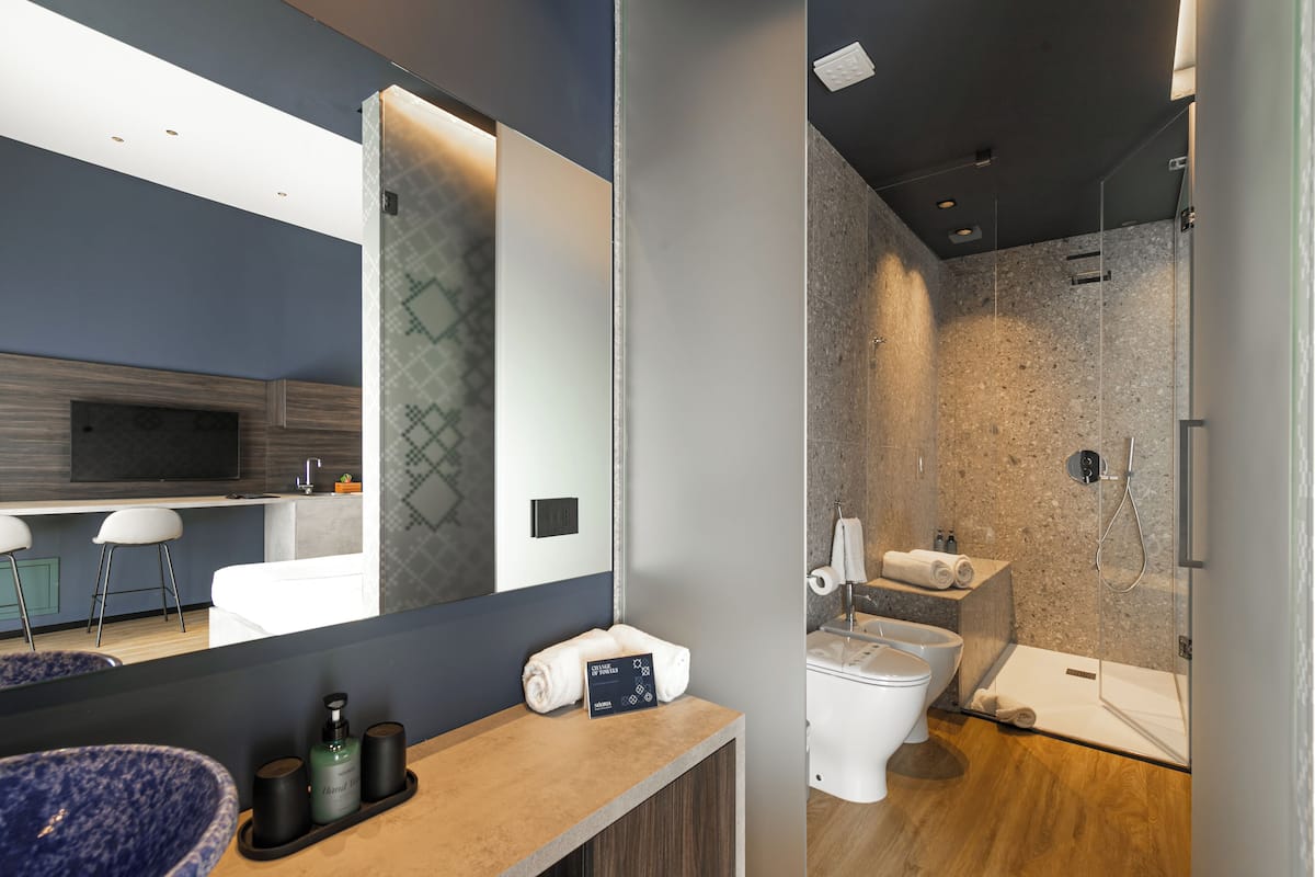 Ein modernes Badezimmer mit großem Spiegel, Waschbecken mit blauer Schüssel, Toilette und Duschbereich.