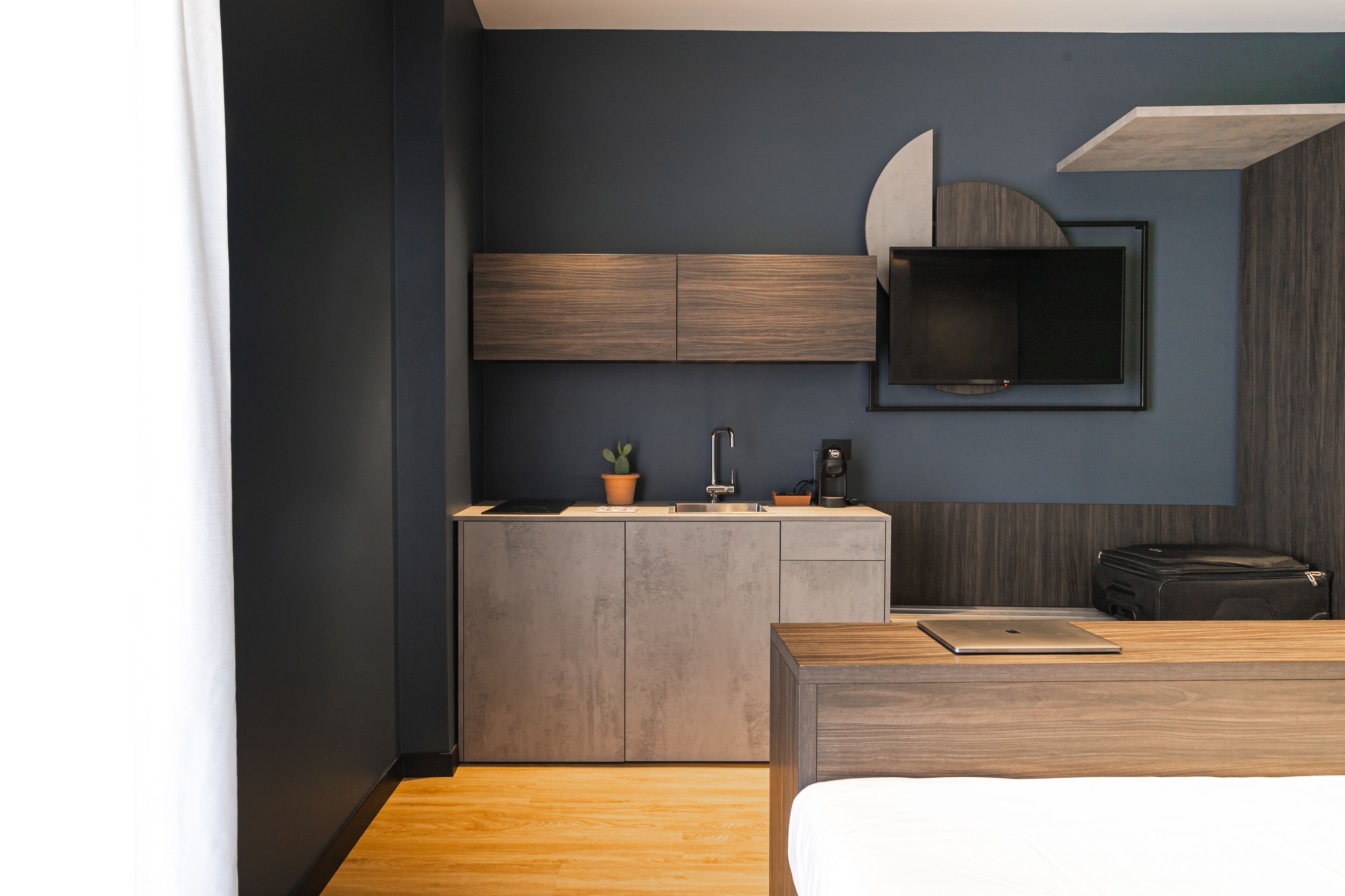 Una habitación de hotel moderna con una cama de madera, una pequeña kitchenette y un televisor de pantalla plana montado en la pared.
