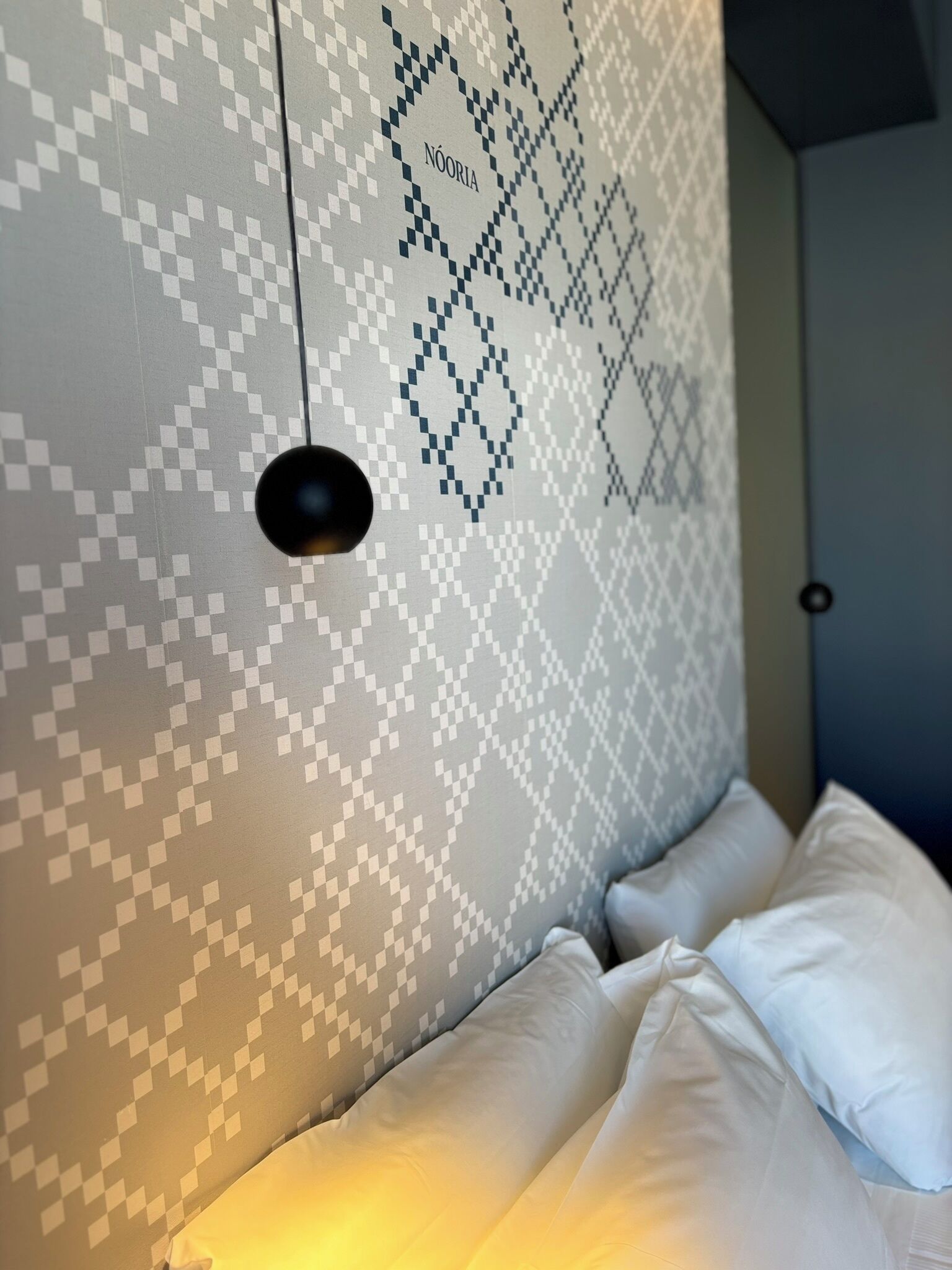A bed with white bedding in a room with a patterned wall and a hanging light fixture.