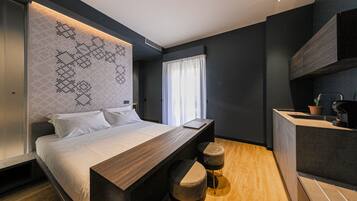 Een moderne slaapkamer met een groot bed, een houten bureau en een geïntegreerd keukenhoekje.