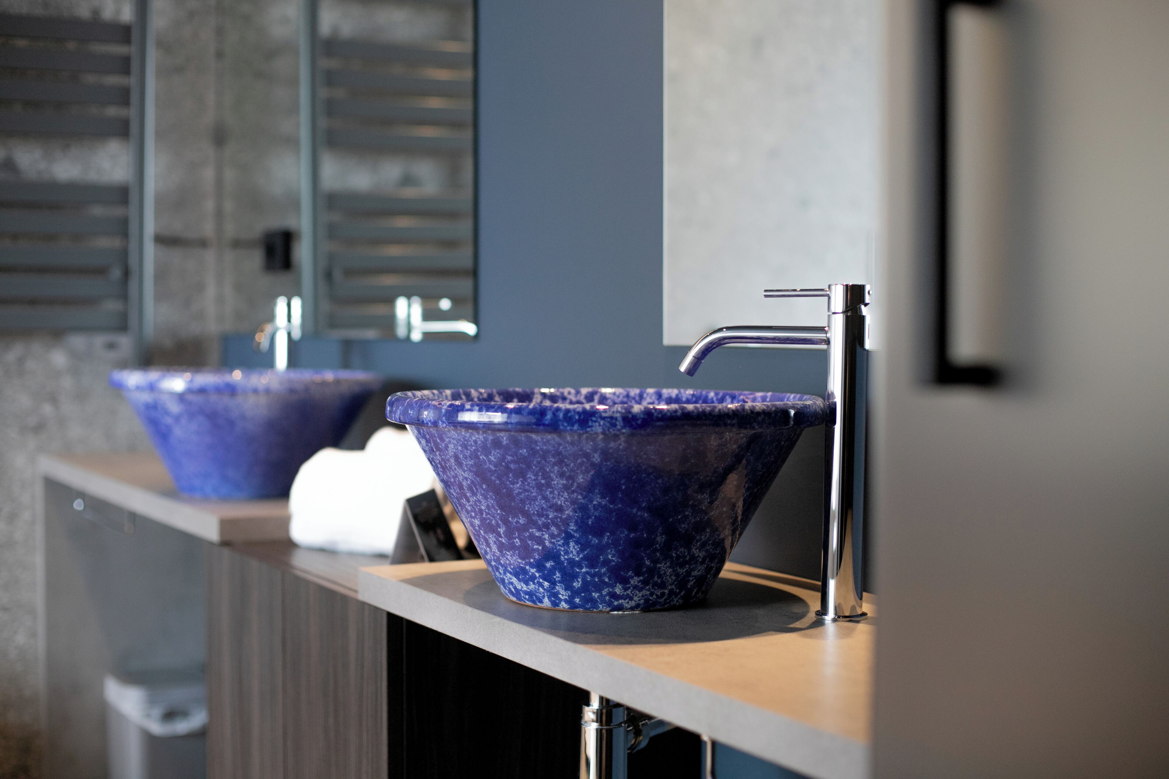A modern bathroom with two blue ceramic sinks, a mirror, and a towel dispenser.