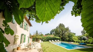 A well-maintained garden with a swimming pool, a patio with outdoor furniture, and a building with green shutters. - L'Hacienda Occitane- Heated pool- air conditioning (Nègrepelisse)