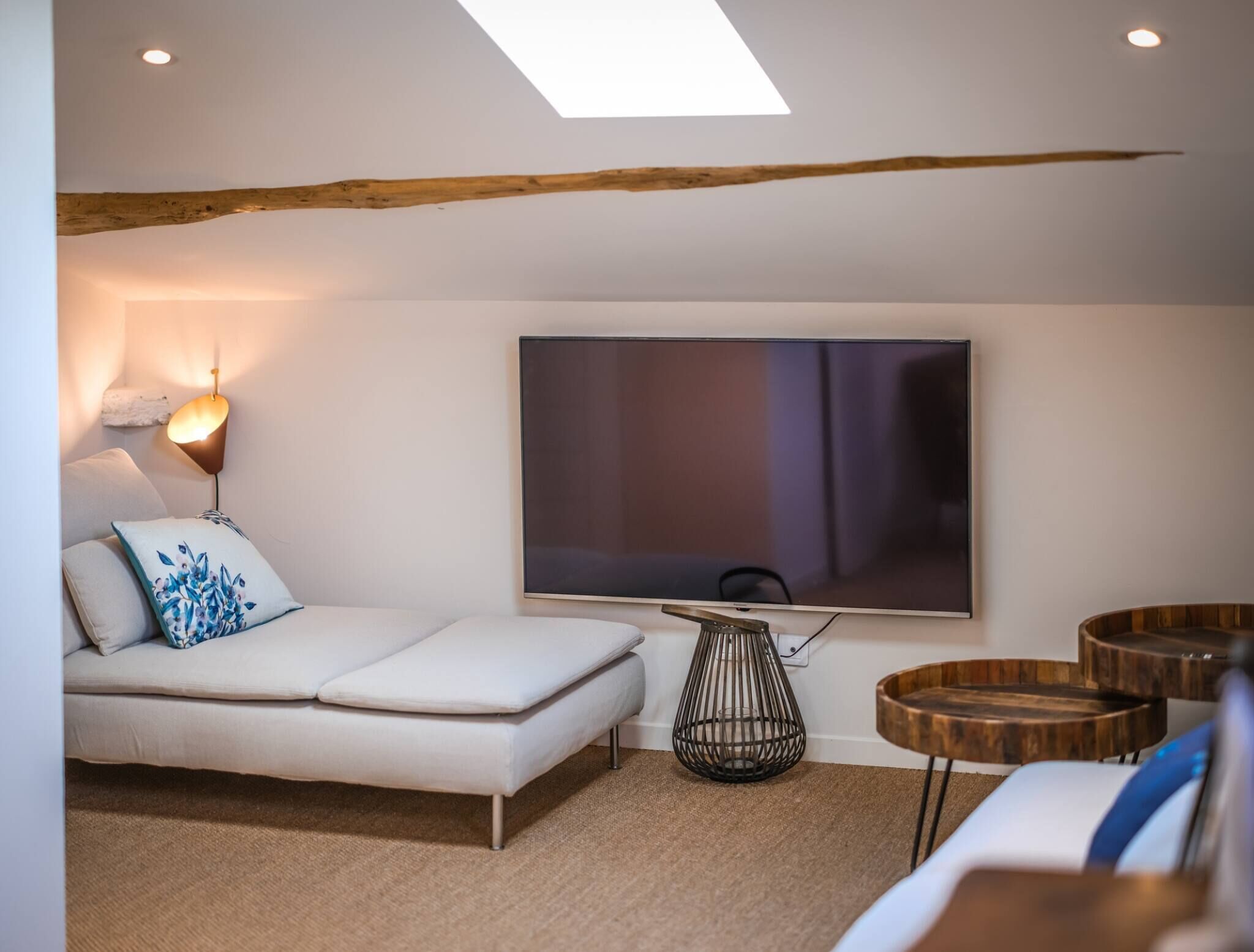 Een moderne woonkamer met een bank, een aan de muur bevestigde televisie, een lamp en een houten balk in het plafond.