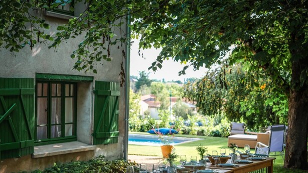 An outdoor dining area with a wooden table set for a meal, surrounded by green chairs and benches. - L'Hacienda Occitane- Heated pool- air conditioning (Nègrepelisse)